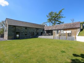 A stone building with multiple windows and doors on a green lawn with a patio and outdoor furniture at Ysgubor Maen Y Bardd in Rowen near Conwy