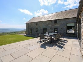 An outdoor patio with a dining table and chairs next to a stone building with a lawn and hills in the background at Ysgubor Maen Y Bardd in Rowen near Conwy