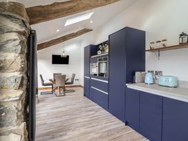 A kitchen area with blue cabinets and appliances next to a dining area with a glass table and four chairs at Gaerau Bach in Llanaber