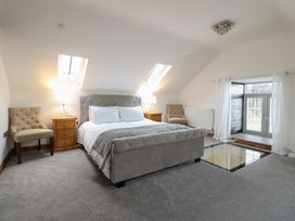 A bedroom with a bed, two chairs, nightstands with lamps, skylights, and a glass floor panel at Gaerau Bach in Llanaber