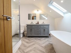 A bathroom with a gray cabinet double sink mirrors toilet shower and freestanding bathtub at Gaerau Bach in Llanaber