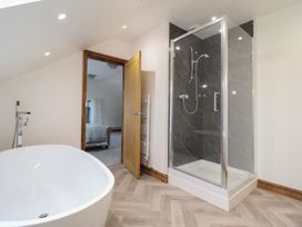A bathroom with a freestanding bathtub a shower enclosure and an open door showing a bedroom at Gaerau Bach in Llanaber
