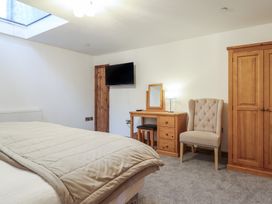 A bedroom with a bed a wooden wardrobe a small desk with a mirror and lamp an upholstered armchair and a wall mounted television at Gaerau Bach in Llanaber