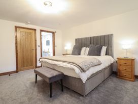 A bedroom with a double bed pillows bench bedside tables lamps and wooden door at Gaerau Bach Llanaber