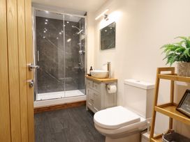 A bathroom with a shower enclosure sink toilet and wooden shelving at Gaerau Bach in Llanaber