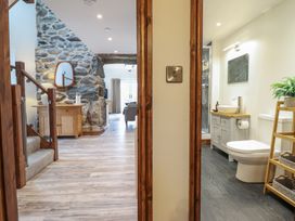 A hallway with stairs and a stone wall on the left and a bathroom with a toilet and sink on the right at Gaerau Bach in Llanaber