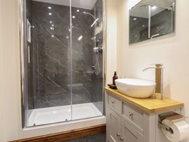 A bathroom with a glass shower enclosure and a sink with wooden countertop at Gaerau Bach in Llanaber