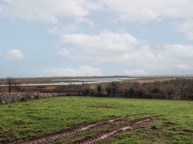 A green field with muddy tire tracks and a stone wall near water and trees at Gaerau Bach in Llanaber