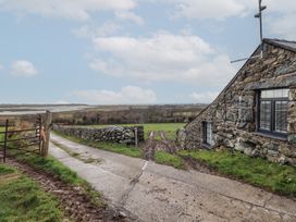 A stone building beside a concrete and dirt driveway with a gate and fields in the background at Gaerau Bach in Llanaber