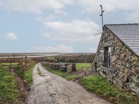 A stone building next to a concrete path with fields and a body of water in the background at Gaerau Bach in Llanaber