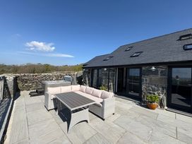 An outdoor patio with a stone floor a rattan sofa set and a hot tub next to a stone building at Gaerau Bach in Llanaber