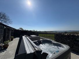 A patio with a hot tub seating area potted plants and stone walls overlooking a field and water at Gaerau Bach in Llanaber