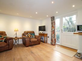 A living room with two leather armchairs a small wooden table a lamp a wall-mounted television a wooden console table with board games floral curtains and a glass door at The Studio at Dan y Garn in Newport Pembrokeshire