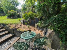 A green metal table and chairs set on gravel near steps beside a garden with plants and rocks at The Studio at Dan y Garn in Newport Pembrokeshire