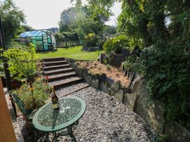 A garden with stone steps leading to a greenhouse and a metal table with a bottle and glasses at The Studio at Dan y Garn in Newport Pembrokeshire