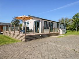 A single-story lodge with a raised deck and glass railing with outdoor furniture and umbrella at 32 Sanctuary Lodge in Y Ffor