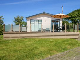 A small house with a deck featuring outdoor furniture and an umbrella at 32 Sanctuary Lodge in Y Ffor