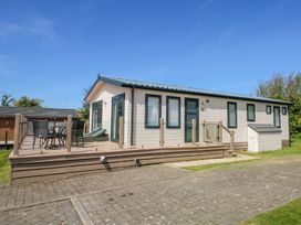 A modern single-story lodge with a deck featuring outdoor furniture at 32 Sanctuary Lodge in Y Ffor