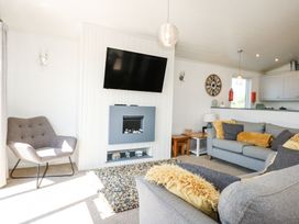 A living room with a gray armchair a mounted TV a fireplace two gray sofas with cushions a clock on the wall and a window at 32 Sanctuary Lodge in Y Ffor
