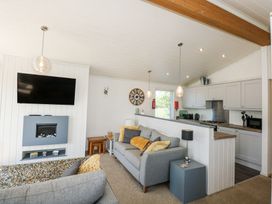 A living room with gray sofas a wall-mounted television and an open kitchen at 32 Sanctuary Lodge in Y Ffor