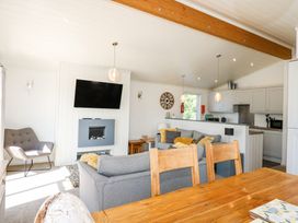 A living room with gray sofas a wooden dining table a wall-mounted TV and a kitchen in the background at 32 Sanctuary Lodge in Y Ffor