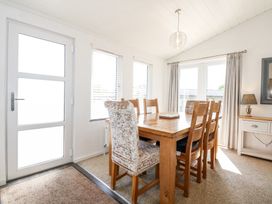 A dining room with a wooden table and six chairs near windows and a door at 32 Sanctuary Lodge in Y Ffor