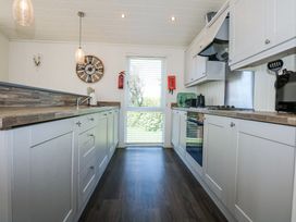 A kitchen with white cabinets wooden countertops a clock on the wall and a window with blinds at 32 Sanctuary Lodge in Y Ffor