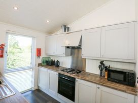 A kitchen with white cabinets a gas stove an oven a microwave and kitchen utensils at 32 Sanctuary Lodge in Y Ffor