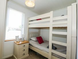 A bedroom with a white bunk bed a bedside table with a lamp and window blinds at 32 Sanctuary Lodge in Y Ffor