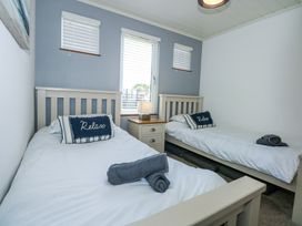 A bedroom with two single beds a bedside table with a lamp and windows with blinds at 32 Sanctuary Lodge in Y Ffor