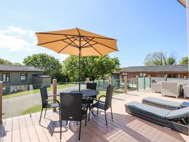 An outdoor deck with a round table and chairs under an umbrella and lounge chairs at 32 Sanctuary Lodge in Y Ffor