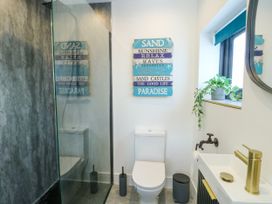 A bathroom with a shower, toilet, sink, and decorative wall sign at Iscoed in Rhosneigr