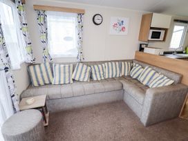 A living room with a gray sectional sofa with striped cushions a small side table an ottoman and windows with patterned curtains at B15 Ty Gwyn in Towyn