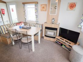 A dining area with a table and chairs beside a corner sofa a TV on a stand and a fireplace with a clock above at B15 Ty Gwyn in Towyn