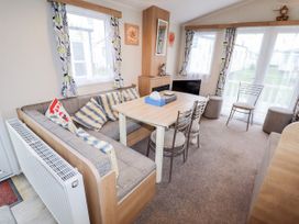 A living room with a corner sofa, dining table with chairs, and windows with patterned curtains at B15 Ty Gwyn in Towyn