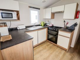 A kitchen with white and wood cabinets a black countertop a microwave toaster kettle stove and a sink at B15 Ty Gwyn in Towyn