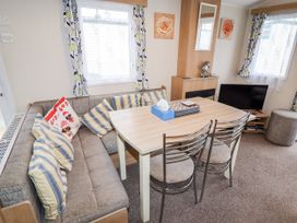 A dining area with a table surrounded by a corner sofa and two chairs next to a fireplace and television at B15 Ty Gwyn in Towyn