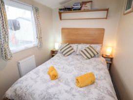 A bedroom with a double bed two bedside tables with lamps a wall shelf with books and pillows and a window with patterned curtains at B15 Ty Gwyn in Towyn
