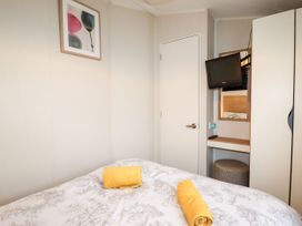 A bedroom with a bed with rolled yellow towels a wall-mounted TV a small desk and a wardrobe at B15 Ty Gwyn in Towyn