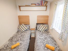 A bedroom with two single beds with patterned bedspreads a bedside table a wall shelf with books and a window with patterned curtains at B15 Ty Gwyn in Towyn