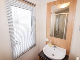 A bathroom with a sink a mirror and a window with blinds at B15 Ty Gwyn in Towyn