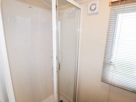 A shower cubicle with glass doors next to a window with blinds in a bathroom at B15 Ty Gwyn in Towyn