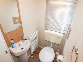 A small bathroom with a white pedestal sink a mirror a white toilet a toilet paper holder and a window with blinds at B15 Ty Gwyn in Towyn