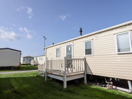 Several beige mobile homes with small porches on grass under a blue sky at B15 Ty Gwyn in Towyn