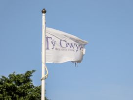 A white flag with ty gwyn holiday park text on a flagpole against a clear blue sky with some tree branches visible at b15 ty gwyn in towyn