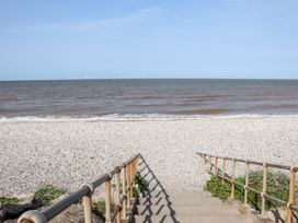 A view down concrete steps with metal railings onto a pebbled beach and the sea with wind turbines on the horizon at B15 Ty Gwyn in Towyn