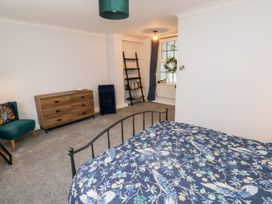 A bedroom with a bed covered with blue floral patterned bedding a wooden dresser a green chair a black ladder shelf and a window at 1 Ilsham Cottages Torquay
