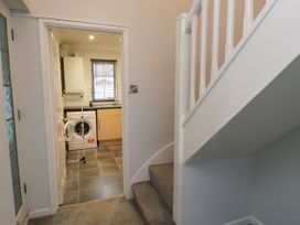 A hallway with carpeted stairs leading up and a doorway opening into a kitchen with a washing machine and a drying rack at 1 Ilsham Cottages in Torquay