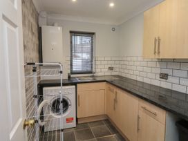 A kitchen with wooden cabinets a washing machine a window with blinds and tiled backsplash at 1 Ilsham Cottages in Torquay