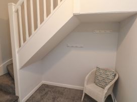 A small corner under a staircase with a white woven chair and two wall-mounted coat racks at 1 Ilsham Cottages in Torquay